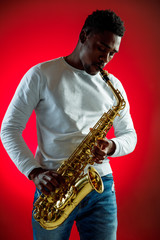 African American handsome jazz musician playing the saxophone in the studio on a neon background. Music concept. Young joyful attractive guy improvising. Close-up retro portrait.