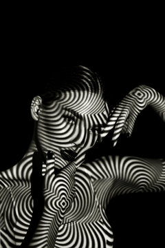 Fototapeta Black and white portrait of a beautiful young girl with a shadow pattern on the face and body in the form of stripes.