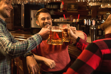 Group of cheerful male friends drinking beer at the bar