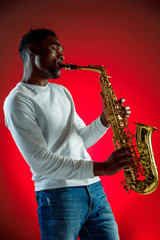African American handsome jazz musician playing the saxophone in the studio on a neon background....