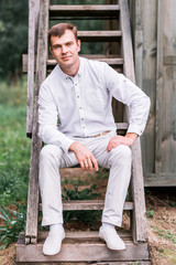 Fototapeta premium The groom in white suit posing on the old wooden stairs