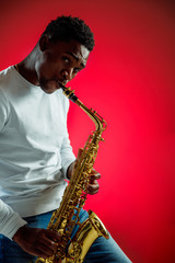 Fototapeta na wymiar African American handsome jazz musician playing the saxophone in the studio on a neon background. Music concept. Young joyful attractive guy improvising. Close-up retro portrait.