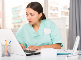 Practicioner girl in medical uniform is working at  laptop