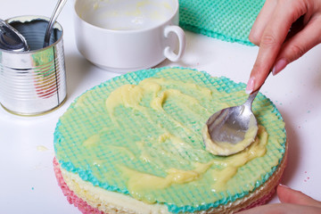 A woman lubricates the cakes and puts in a pile. Round wafer cakes of different colors. For making waffle cake. Nearby there is a can of condensed milk to soak the cakes.