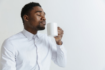 Coffee makes his day. Young handsome African man drinking coffee and looking away while sitting at his working place