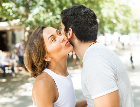 cheerful adult man and woman meeting and kissing on the street