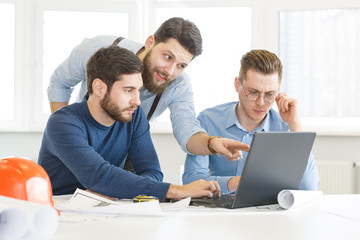 Professional architects working on building plans together using laptop