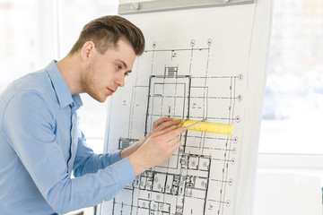 Naklejka na ściany i meble Handsome architect working on blueprint at his workspace