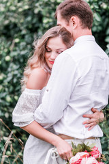 Bride and groom with a bouquet of peonies posing against the backdrop of the forest