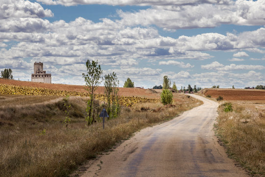 Un paisaje castellano de campo de trigales cruzado por una carretera y con un cielo lleno de nubes