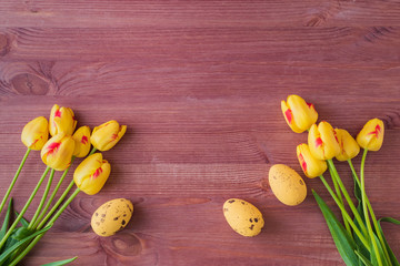 Flat lay composition with yellow tulips and easter eggs on a wooden background