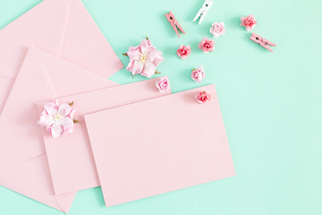Flowers composition romantic. Pink envelopes and flowers on pastel mint background. Flat lay, top view, copy space