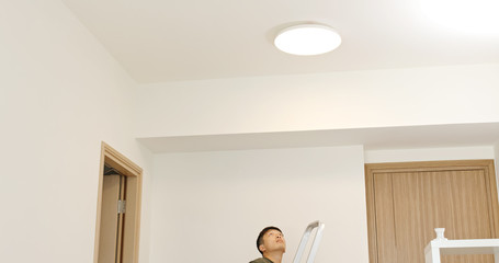 Asian Man install lamp onto the ceiling at home
