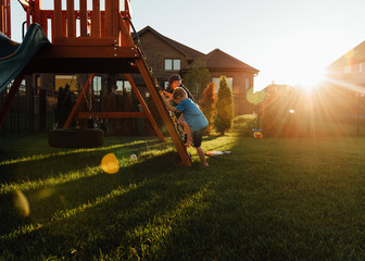 Brother playing on slide in backyard during sunset