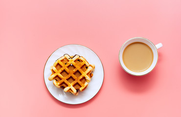 A cup of coffee with milk and homemade waffles on a pink background. Tasty breakfast. Minimalism