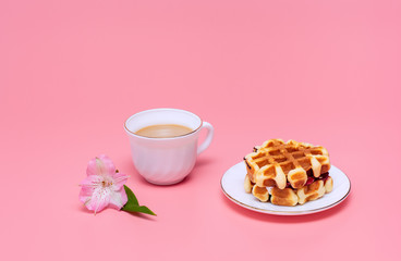A cup of coffee with milk and homemade waffles on a pink background. Tasty breakfast. Minimalism