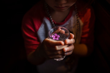 Midsection of girl holding drinking glass with flower in darkroom