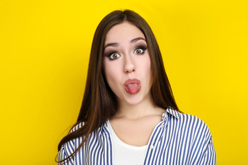 Beautiful young woman showing tongue on yellow background