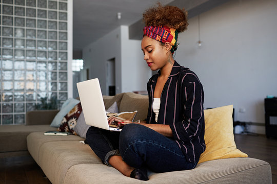 Young american african female blogger working remotely on digital netbook with internet text. African woman copywriter typing article for website on keyboard of modern laptop computer at home.