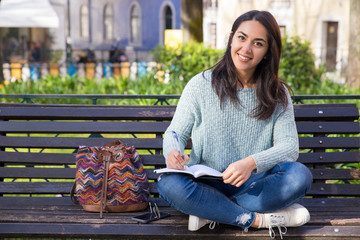 Happy woman making notes and sitting on bench outdoors