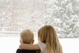 Rear view of siblings looking through window during winter