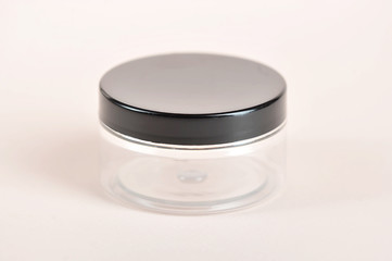 Plastic transparent jar with a black lid for cosmetic cream or gel. Light background. Close-up. Side projection.