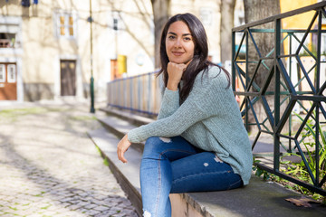 Smiling pretty young woman sitting on stone bench outdoors