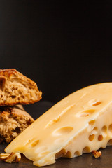 A delicious piece of Swiss cheese with bread and nuts on dark background.