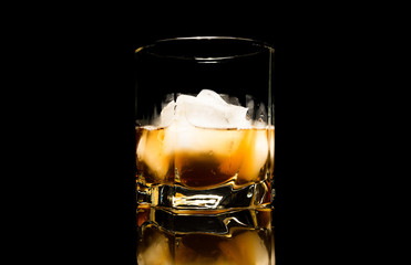 Whiskey with ice close up on a glass table isolated on a black background