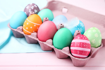 Colorful easter eggs in carton box on pink wooden table
