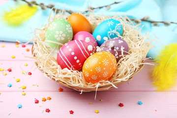 Colorful easter eggs in basket with sprinkles on pink wooden table