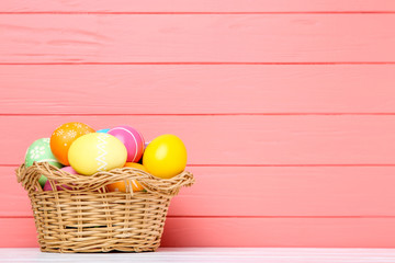 Colorful easter eggs in basket on coral wooden background