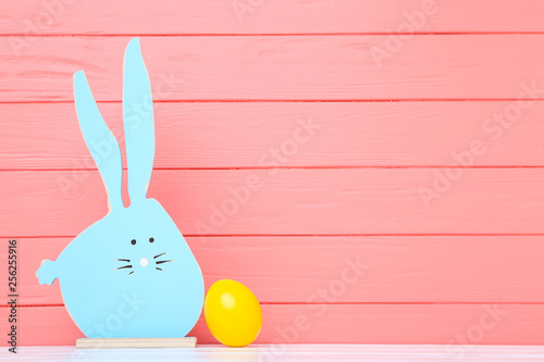 Colorful easter egg with wooden rabbit on coral color background