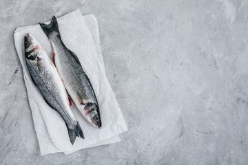 Fresh raw fish sea bass (seabass) with sea salt on gray stone background.