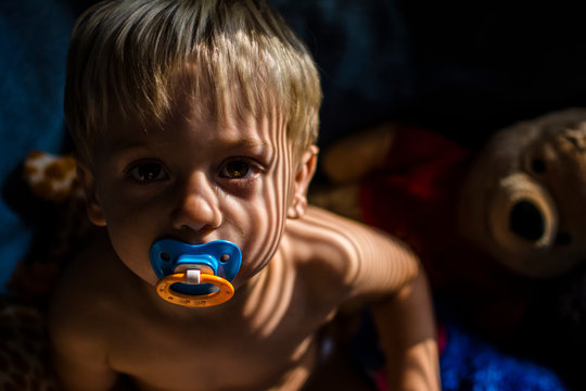 Portrait of shirtless boy with pacifier in mouth at home