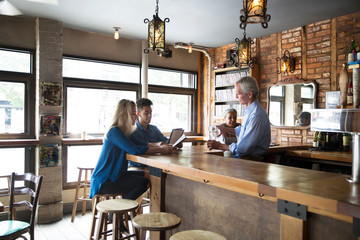 Smiling owner talking to customer while standing at bar counter in cafe