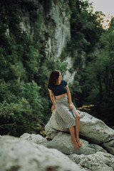 Young and sexy woman sit on rock wearing swimsuit on the beautiful waterfall in the jungle beside cliff