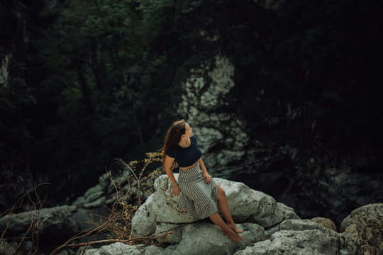 Young and sexy woman sit on rock wearing swimsuit on the beautiful waterfall in the jungle beside cliff