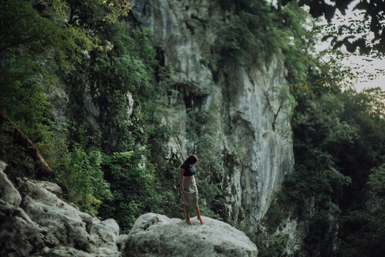 Young and sexy woman sit on rock wearing swimsuit on the beautiful waterfall in the jungle beside cliff