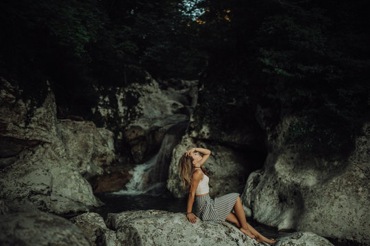 Young and sexy woman stay on rock wearing swimsuit on the beautiful waterfall in the jungle beside waterfall