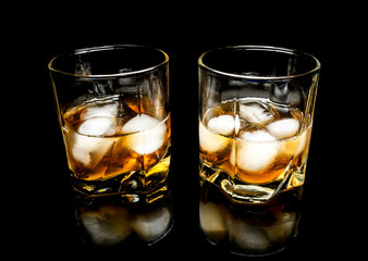 Whiskey with ice close up on a glass table isolated on a black background