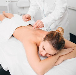 Acupuncturist inserting a needle into a female back. patient having traditional Chinese treatment using needles to restore an energy flow through specific points on the skin.