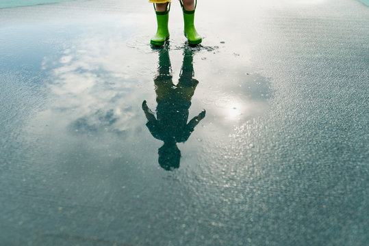 Reflection of boy in rubber boots standing in puddle