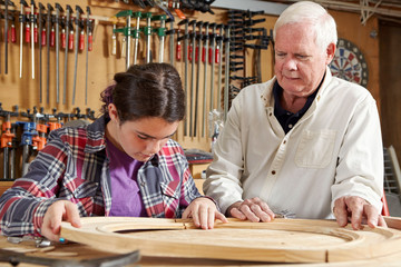 Carpenter teaching girl in workshop
