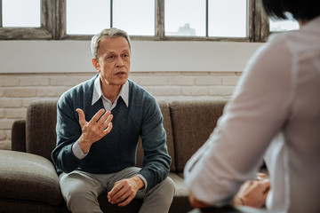 Active grey-haired man in blue cardigan explaining his feeling to woman