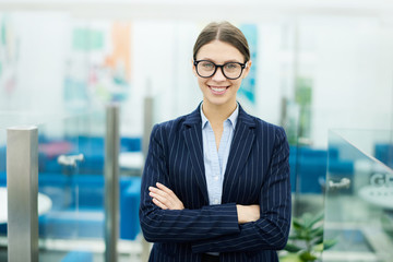 Waist up portrait of smiling young businesswoman standing with arms crossed and looking at camera, copy space
