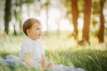 little stylish blond  boy with blue eyes dressed in a white shirt playing outside