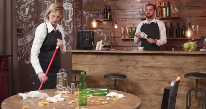 Waitress brooming the floor after a busy work day. Employees preparing to close the resturant after all the customers left a big mess.