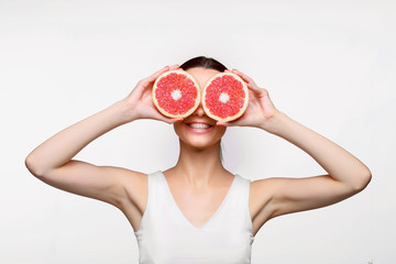 Portrait of young happy beautiful woman with healthy perfect smooth skin holds two pieces of grapefruit, closing two eyes. Natural cosmetics, skincare, wellness, facial treatment, cosmetology concept.
