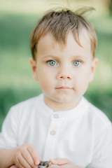 Portrait of a young boy with light hair and blue eyes in a white shirt against a green forest background
